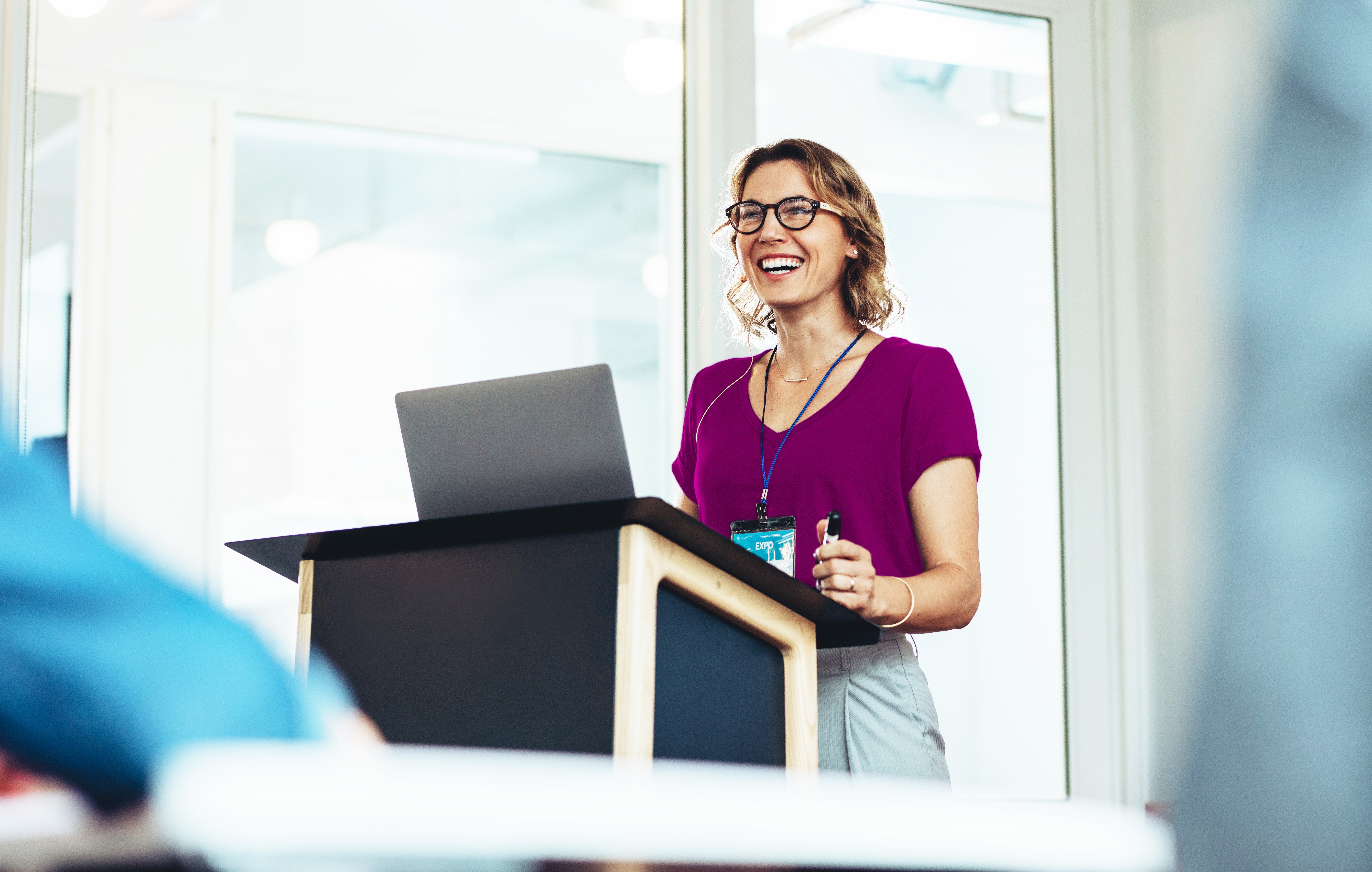 Woman stands at podium smiling and giving lecture
