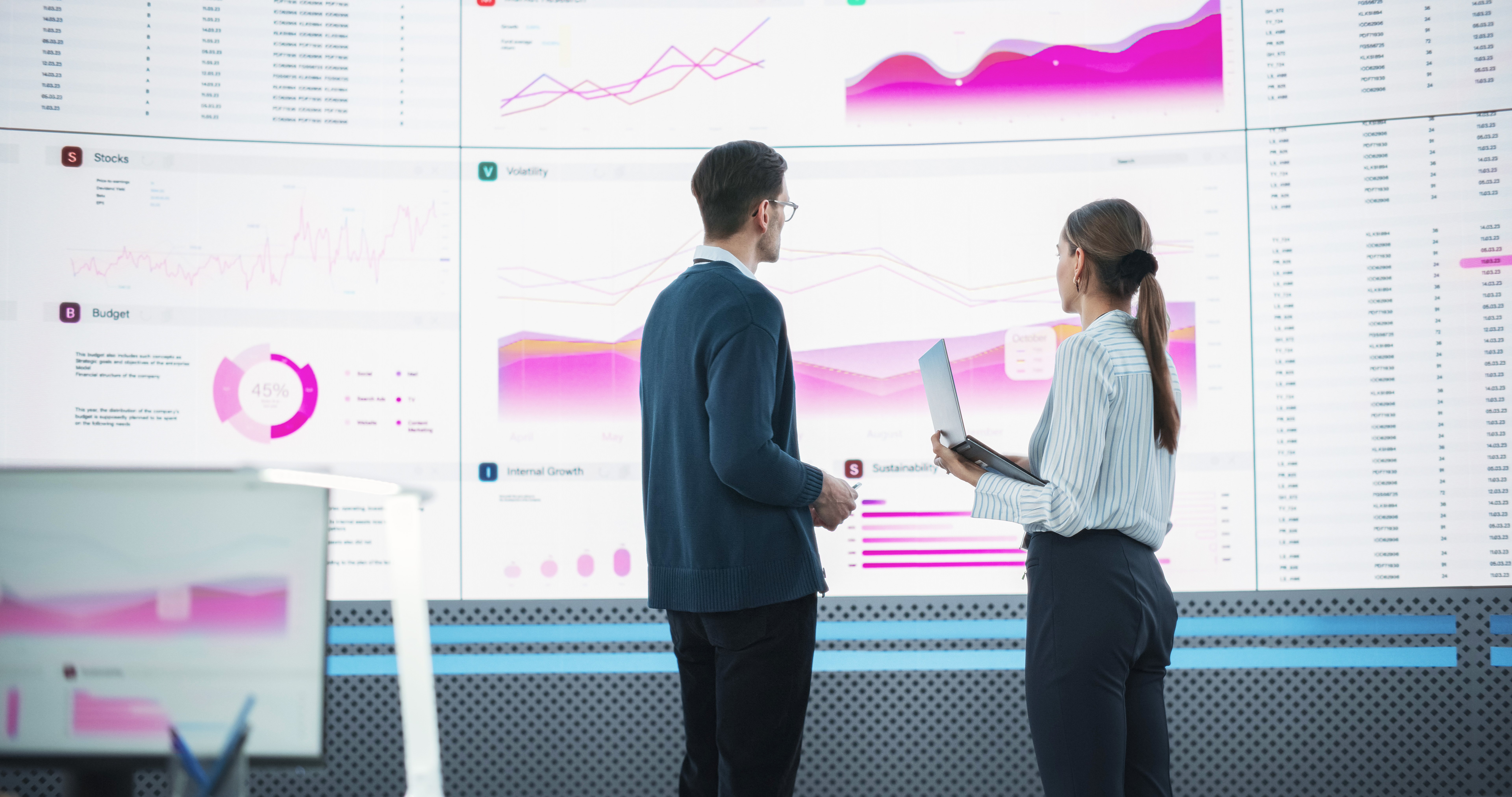 Back View Following Shot Of Male And Female Analysts Discussing Data On Big Digital Screen In Monitoring Office